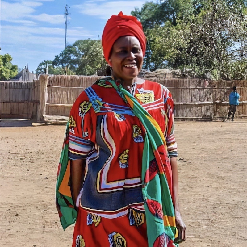 A woman in bright colours smiling, with a wooden fence in the background.