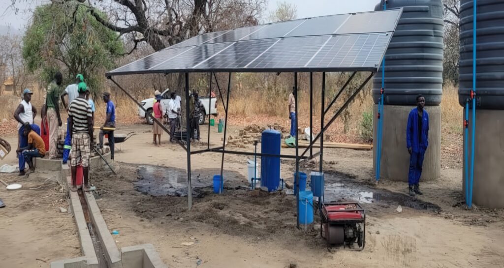 Solar panels, water tanks and people drawing water.
